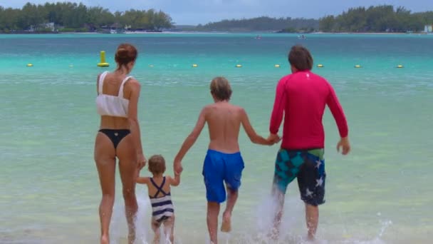 Eltern und Kinder in Badeanzügen laufen in den Sommerferien im Meer. Ferienkonzept. — Stockvideo