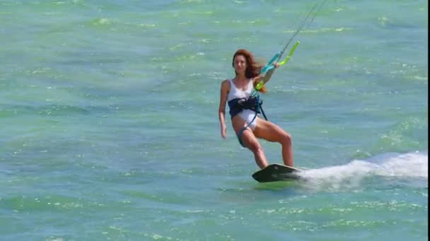 Una hermosa joven en un traje de baño blanco monta las olas en una cometa en un océano limpio y transparente — Vídeos de Stock