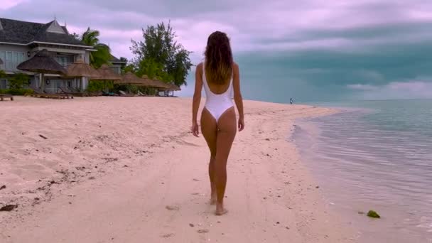 Widok z tyłu pięknej kobiety w białym bikini. Spacerując po piaszczystej plaży rajskiej plaży wyspy. Film w zwolnionym tempie — Wideo stockowe