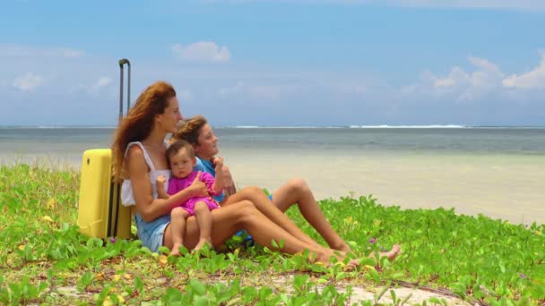 Kobieta z rodziną i żółtą walizką na plaży — Wideo stockowe