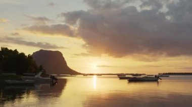 Zaman aşımı: Mauritius gün batımında denizde yüzen balıkçı tekneleri, bulutlu tropikal hava, renkli gökyüzü ve ufukta dağ profili.