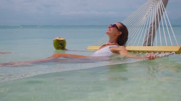 Une belle fille en maillot de bain blanc se détend tout en étant allongée dans un hamac et boit une noix de coco. Plage vacances concept de luxe océan Indien. Maurice. — Video