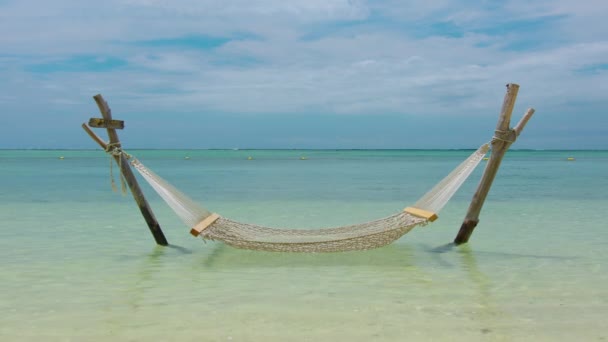 Static shot of an empty hammock slowlying by the wind with calm waves reaching the shore from the ocean. Indian ocean. Maldeves. — стокове відео