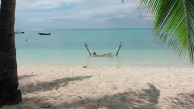 Üst Manzara. Beyaz mayo giymiş bir kız hamakta yatarken rahatlıyor. Sahil tatili konsepti Hint okyanusu. Mauritius.