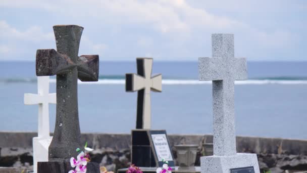 Crosses gravestones stand on the rocky shore as waves crash over the rocks. Oceanfront cemetery — Stockvideo