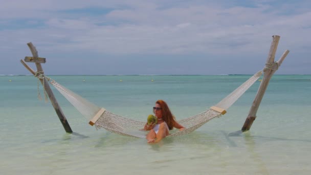 Una muchacha hermosa en un traje de baño blanco relaja mientras que miente en una hamaca y bebe un coco. Playa vacaciones concepto de lujo Océano Índico. Mauricio. — Vídeos de Stock