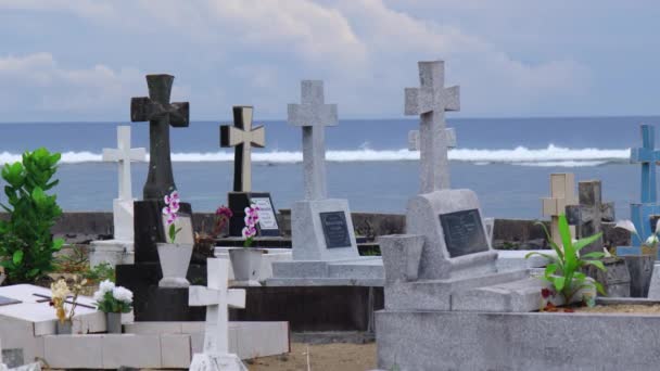 Crosses gravestones stand on the rocky shore as waves crash over the rocks. Oceanfront cemetery — Stockvideo