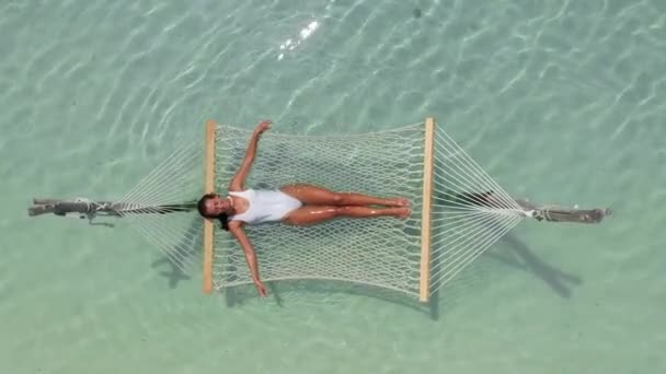 An attractive girl lies in a hammock in the middle of the Indian Ocean in the clear water enjoying her vacation. Top view — Stockvideo