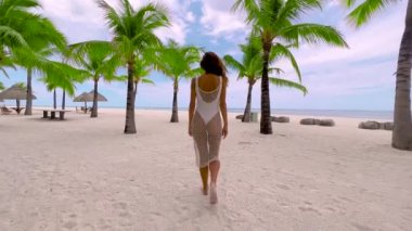 Mauritius, Hint Okyanusu plajı, kadın palmiye ağaçlarının yanında dinleniyor. Deniz kıyısındaki güzel kız güneşli yaz gününde dinleniyor. Efsanevi tropik tatil köyü. 4K 'da sinematik çekim