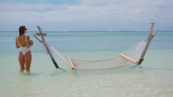 Mulher de biquíni branco relaxa em uma rede sobre águas tropicais turquesa. Conceito de luxo para férias na praia. Oceano Índico. — Vídeo de Stock