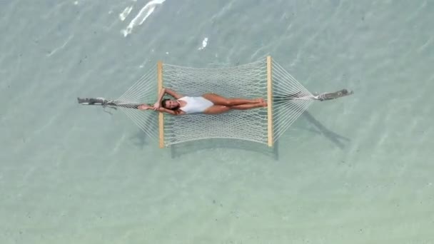 An attractive girl lies in a hammock in the middle of the Indian Ocean in the clear water enjoying her vacation. Top view — Video