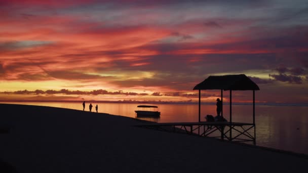 Zonsondergang, pier. Tropische avondvideo met aanlegsteiger en kalme oceaan. Silhouet van de mensen op het strand — Stockvideo