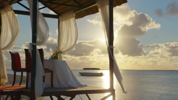 Table par la mer avec des collations sucrées, boissons pour banquet à l'air frais à l'extérieur. Sur nappe blanche décorée de plats à fleurs jaunes, vases avec décorations, verres divers — Video