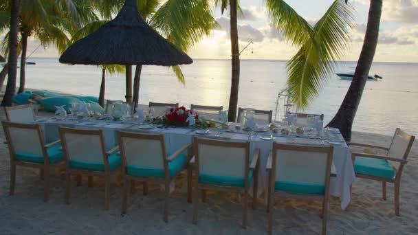 Mesa junto al mar con dulces aperitivos, bebidas para banquetes al aire libre. Sobre mantel blanco decorando con platos de flores amarillas, jarrones con decoraciones, varios vasos — Vídeo de stock