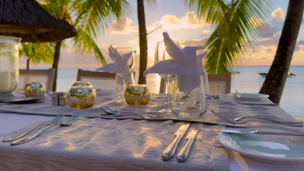 Table par la mer avec des collations sucrées, boissons pour banquet à l'air frais à l'extérieur. Sur nappe blanche décorée de plats à fleurs jaunes, vases avec décorations, verres divers — Video