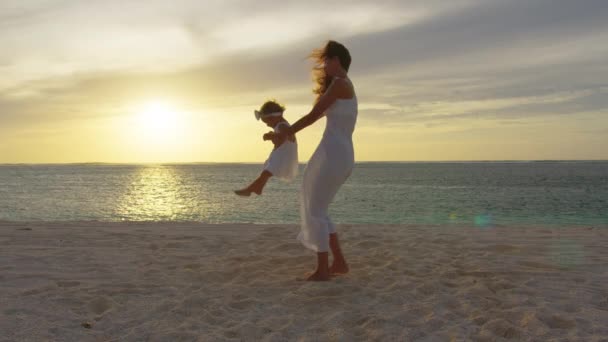 妈妈在海滩上旋转着他的女儿,在日落时玩得很开心.妈妈在水边和孩子玩耍。快乐的家庭和童年的概念。母亲和健康的孩子在阳光下飞翔的轮廓 — 图库视频影像