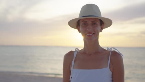 Portret van een jonge vrouw met een hoed op het strand. Mooie vrouwelijke gelukkig ontspannen wandelen op het strand in de buurt van de zee bij zonsondergang in de avond. Lifestyle vrouwen reizen op strand concept — Stockvideo