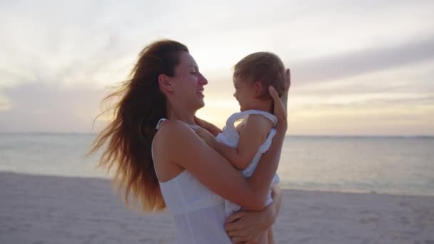Auténtica toma de cerca de una madre joven es mantener en sus brazos y jugar con un bebé recién nacido en una playa junto al mar al atardecer durante las vacaciones de vacaciones — Vídeo de stock