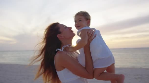 Mama wyrzuca jego szczęśliwą córeczkę w powietrze na plaży, bawiąc się o zachodzie słońca. Szczęśliwa koncepcja rodziny i dzieciństwa. Sylwetka matki i zdrowego dziecka latającego nad słońcem. — Wideo stockowe