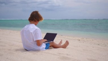 Bir öğrenci, turkuaz suyun arka planında oturarak kendini eğitmekle meşgul. Çevrimiçi eğitim kavramı. COVID-19 tecridi sırasında online derse katılan genç bir çocuk.