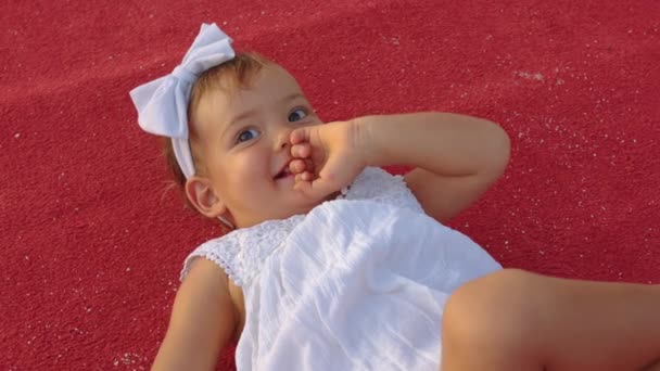 Mała dziewczynka w białej sukience leży na czerwonym dywanie — Wideo stockowe