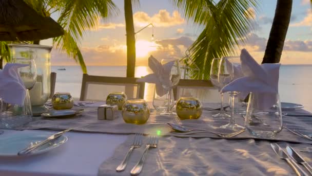 Masă pe mare cu lucruri dulci gustări, băuturi pentru banchet pe aer curat în aer liber. Pe fața de masă albă decorarea cu feluri de mâncare de flori galbene, vase cu decorațiuni, diverse ochelari — Videoclip de stoc