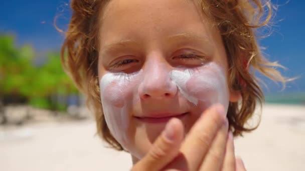 Мама намазывает кремом для лица мальчиков на пляже на берегу моря. Защита от солнца и уход за кожей — стоковое видео