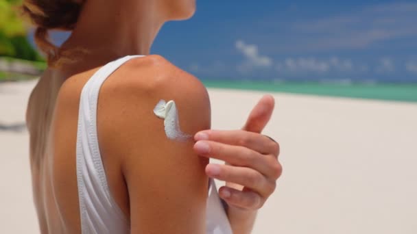 Close up de uma jovem sorridente feliz está aplicando um protetor solar ou bronzeamento loção em um ombro para cuidar de sua pele em uma praia à beira-mar durante as férias. — Vídeo de Stock