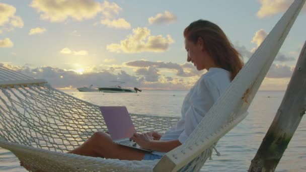 Una mujer joven empresaria utiliza un ordenador portátil para trabajar en la hamaca en el océano. Una mujer de negocios que trabaja profesionalmente para planear el trabajo, sonríe y felicita a su negocio está haciendo bien — Vídeo de stock