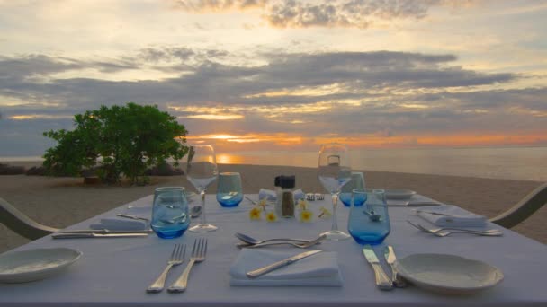 Mauritius 'ta popüler bir seyahat merkezinde günbatımını izlerken plajda romantik bir akşam yemeği için uzanmış masa ve sandalyelerden oluşan bir plajdan POV. — Stok video
