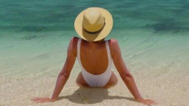 Plaj güneşi tatil konsepti. Beyaz kumlu cennet kumsalındaki kadın. Güneş banyosu yaparken bikini ve güneş şapkası takan bir kadın.
