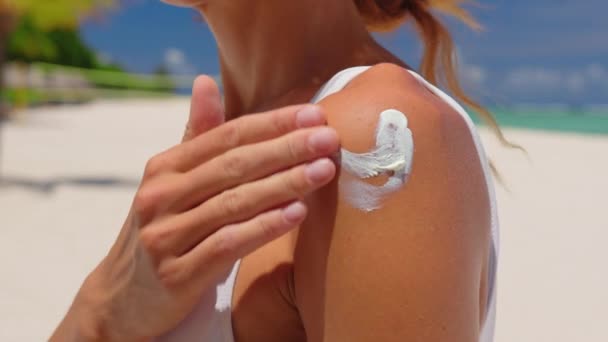 Close up de uma jovem sorridente feliz está aplicando um protetor solar ou bronzeamento loção em um ombro para cuidar de sua pele em uma praia à beira-mar durante as férias. — Vídeo de Stock