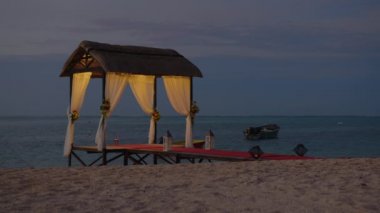 Deniz kıyısına kurulmuş bir düğün kumsalı. Hint Okyanusu kıyısında çiçeklerle süslenmiş bir düğün kemeri. Tatil konsepti. Gün batımında düğün şablonu adası