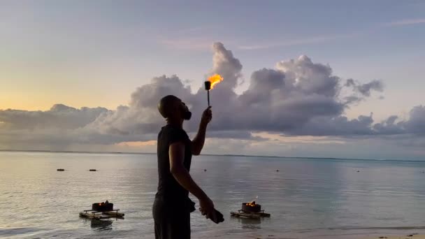 Cool fire show művész tüzet okád a sötét levegőben, lenyűgöző mutatványokat csinál az óceán hátterében — Stock videók