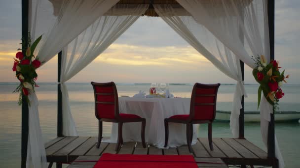 Романтический вечерний стол для двоих на пляже на закате на фоне красивых облаков — стоковое видео