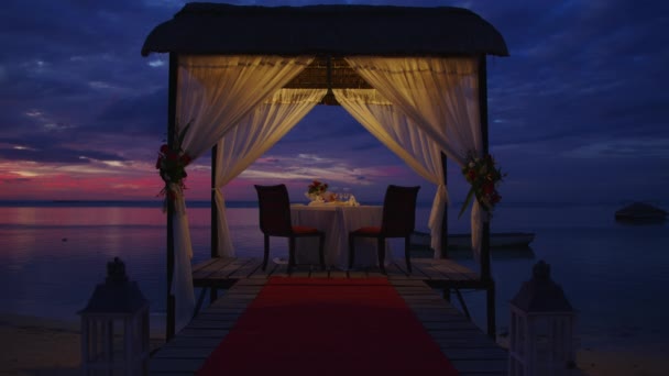 Mesa de noche romántica para dos personas en la playa al atardecer en el fondo de hermosas nubes — Vídeos de Stock