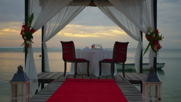 装饰一个节日餐桌。婚桌装饰。夕阳西下，在美丽的云彩衬托下，两个人在海滩上的浪漫餐桌 — 图库视频影像