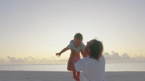 Autentyczne zbliżenie młodego ojca trzyma go na rękach i bawi się z noworodkiem na plaży nad morzem o zachodzie słońca podczas wakacji — Wideo stockowe