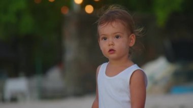 Güzel bir bebeğin yakın portresi. Kumsalda rüzgarda savrulan saçlar ağır çekimde. Gülümsüyor ve çekici.