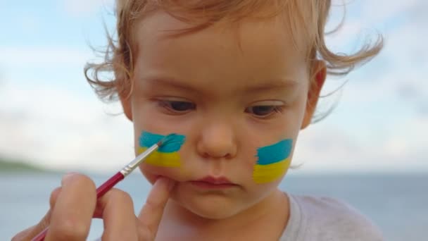 Feche o retrato pequeno bebê com a bandeira da Ucrânia na cara sentado sozinho. Protesto contra a invasão de guerra russa na Ucrânia. Bandeira ucraniana, conceito de protestantes — Vídeo de Stock