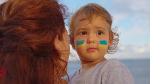 우크라이나 국기 앞에 어린 아기와 엄마의 초상화를 닫으세요. 러시아의 우크라이나 침공에 반대하는 시위. 우크라이나 국기, 단백질 개념 — 비디오