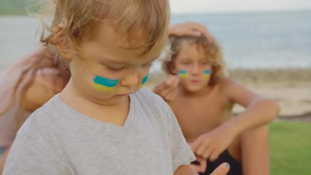 Figli di guerra in Ucraina. Ragazzi e ragazze rifugiati dall'Ucraina guardano al futuro. La bandiera ucraina è dipinta sul volto — Video Stock