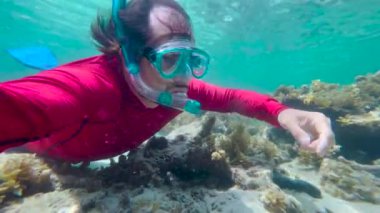 Sualtı maskeli bir adam temiz suda şnorkelle yüzüyor. Hint Okyanusu 'ndaki mercan kayasının yakınındaki sualtı sahnesi dalgıcı..