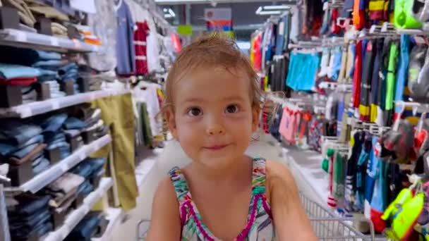 Baby rider i en kundvagn nerför en rad i en stormarknad. Liten flicka njuta familj shopping tillsammans. — Stockvideo