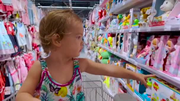 Bebê monta em um carrinho de compras para baixo uma fileira em um supermercado. Menina gosta de compras em família juntos. — Vídeo de Stock