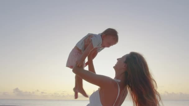 Authentic close up shot of young mother is keeping on her arms and playing with a newborn baby on a seaside beach at sunset during holiday vacation — Stock Video