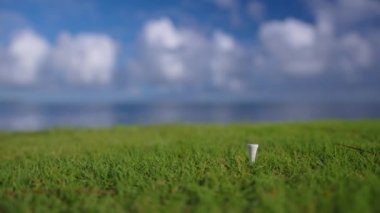 Golf eldivenli bir erkek, topu mavi okyanusun arka planındaki sahaya koyuyor. Kapat.