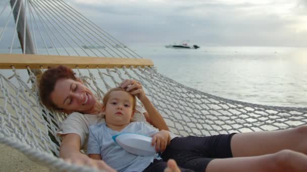 Little girl gently hugs mom in a hammock in a hammock slow motion stock. Baby is resting with a happy mother in a hammock on the ocean. Concept of children, baby, parenthood, childhood, motherhood — Stock Video