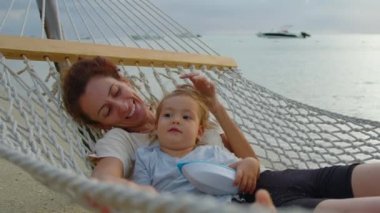 Anne ve kızı mutlu bir aile. Bebek gün batımında okyanusta bir hamakta mutlu bir anneyle dinleniyor. Çocuk, bebek, ebeveynlik, çocukluk, hayat, annelik kavramı