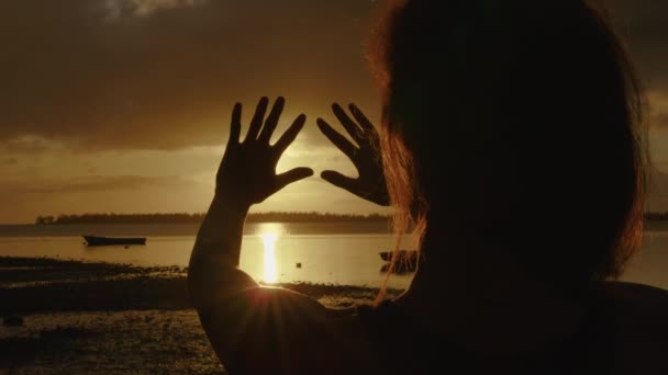Handen van een gelukkig meisje bij zonsondergang. Zonsondergang tussen de handen van een meisje. gelukkig meisje met lang haar dromerig strekt haar hand uit naar de zon — Stockvideo